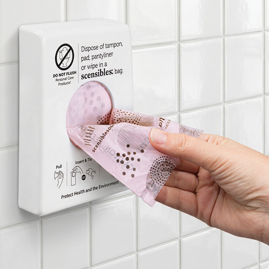 Scensibles disposal bag being removed from a wall-mounted restroom dispenser